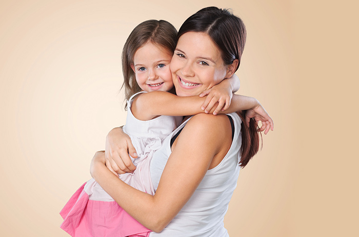 Junge Mutter mit kleinem Mädchen im Arm, beide lächeln und sind glücklich über die Situation.