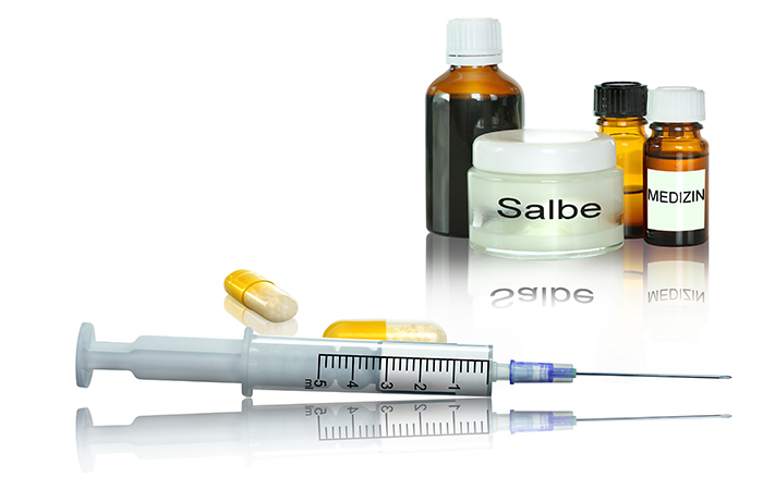 Tabletten, Salbe, Medizinflaschen und Spritze auf weißem leicht spiegelnden Hintergrund als Medikamente zur konservativen Behandlung