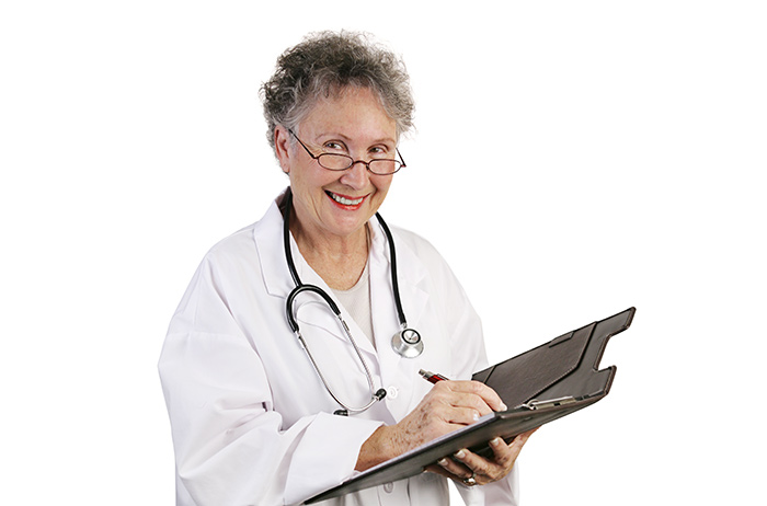 Ältere Frauenärztin mit kurzen, grauen Haaren und Brille macht sich Notizen und schaut dabei fröhlich in die Kamera.