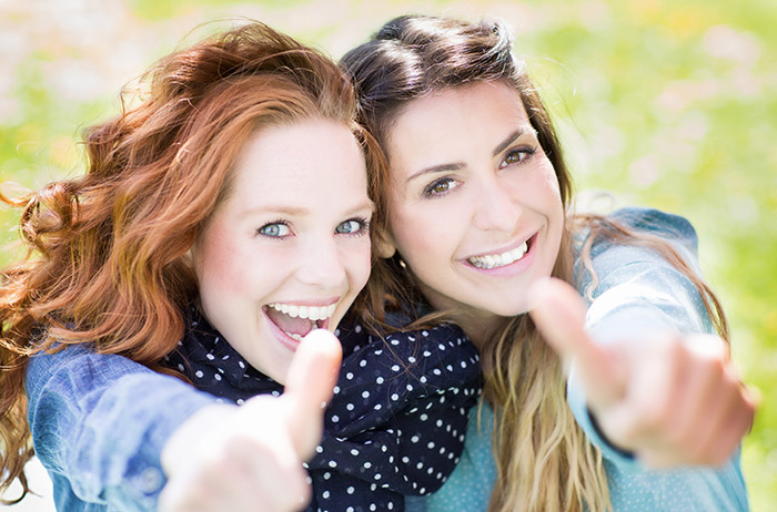 Zwei Frauen mit jeweils rotem und braunem Haar und strahlendem Lächeln halten ihre Daumen hoch für die Vorteile des S-Pap.