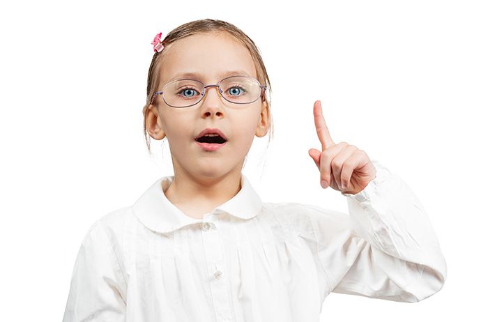 Junges hellwaches 8-jähriges Mädchen mit blonden glatten Haaren und roter Haarspange in weisser Bluse und großer Brille hebt den Zeigefinger der linken Hand nach oben, als wolle sie sagen: Das Wichtige zusammengefasst.