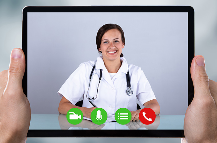 Zwei Hände halten ein Tablet , uaf dem eine Ärztin in einer Videokonferenz zu sehen ist.