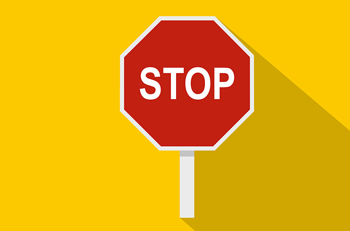 Achteckiges Stopp-Schild auf weißem Pfosten vor gelbem Hintergrund, mit Schattenwurf nach rechts.